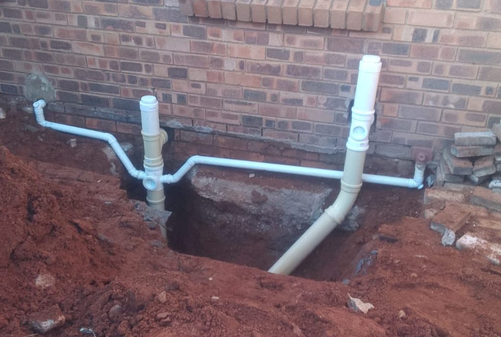 Outdoor drain unblocking work in Midrand, showing a partially dug-up area near a building.