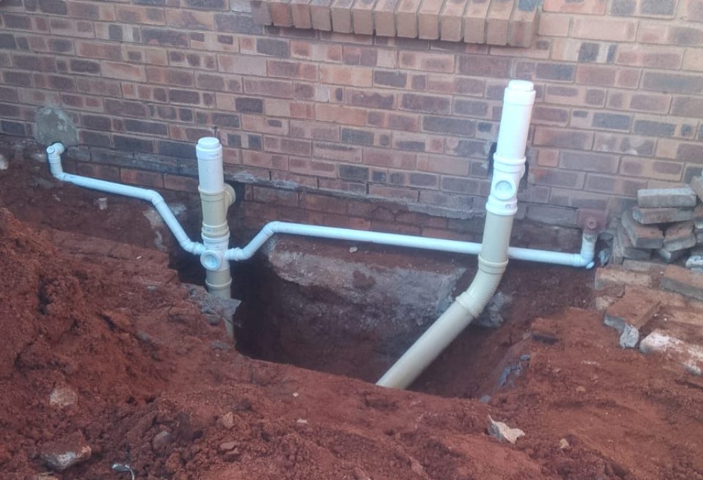 Outdoor drain unblocking work in Midrand, showing a partially dug-up area near a building.