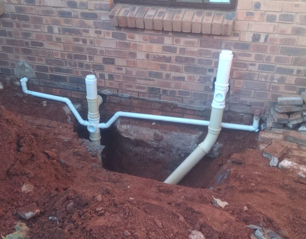 Outdoor drain unblocking work in Midrand, showing a partially dug-up area near a building.